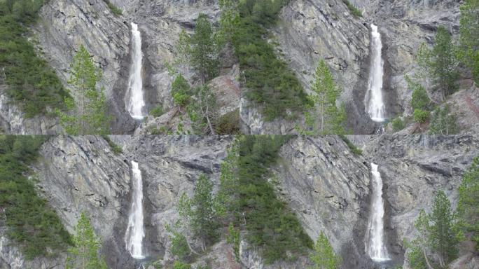 空中无人机镜头在树冠上方缓慢飞行，露出陡峭的瀑布，瀑布从陡峭的山崖边缘飞入瑞士的跳水池。