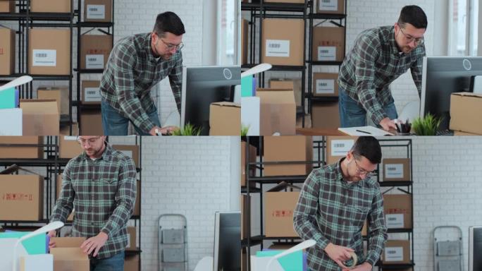 一位男性在线商店老板在仓库的办公桌上的计算机上工作。一名男性工人在一个装满包裹的架子的房间里收拾箱子