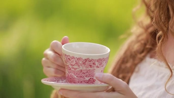 年轻漂亮的女人喝酒，在户外用漂亮的陶瓷杯、茶或咖啡。在夏日晴天野餐。