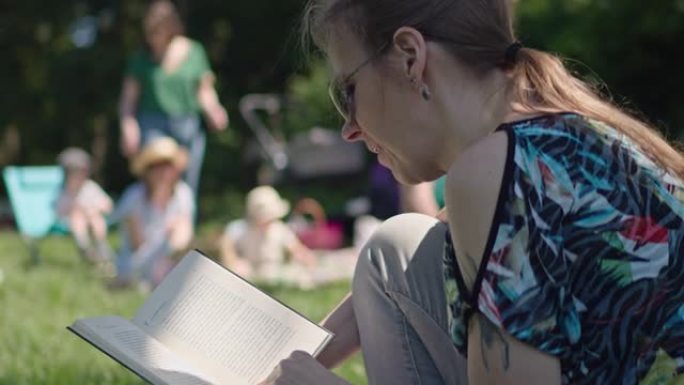 戴着墨镜的女人在公园集体旅行时坐在草地上看书