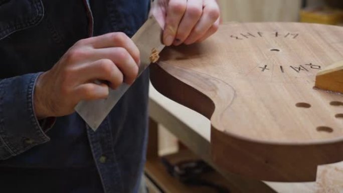吉他制造商使用刮刀工具在车间中平滑雕刻吉他主体的背面