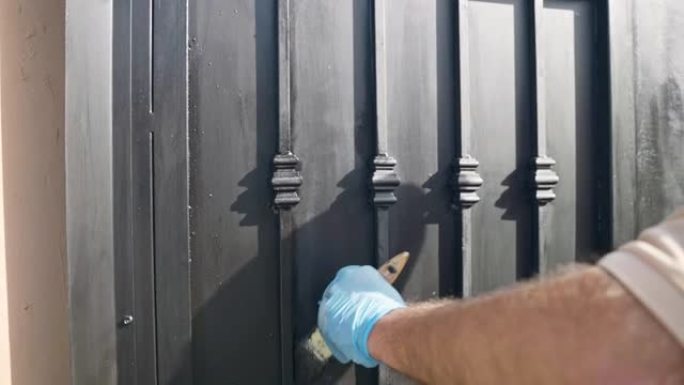 修理工在施工现场用黑色油漆着色钢门，用化学溶液和特殊的维修设备和工具修复旧腐蚀门的过程。穿着一次性手