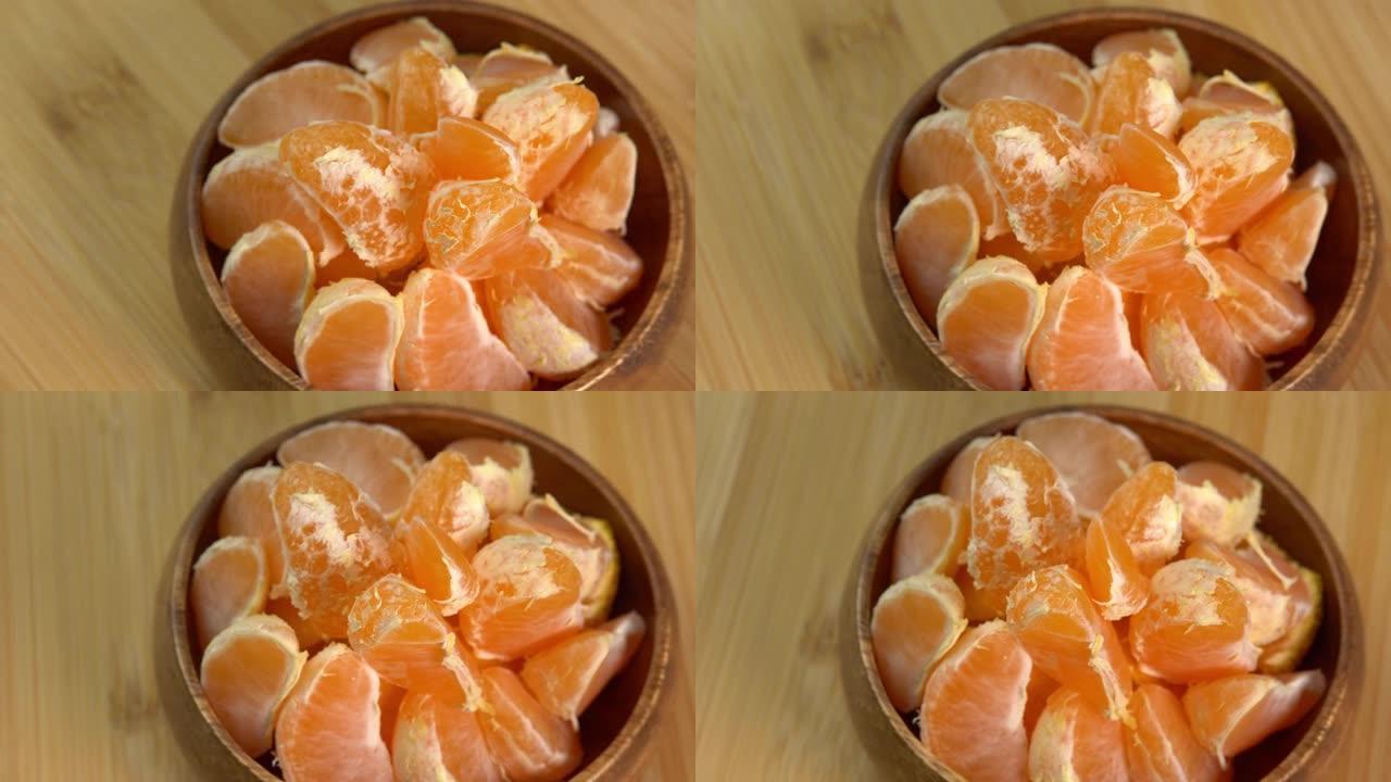 木碗中的橘子在木板上旋转。蜜柑果片特写