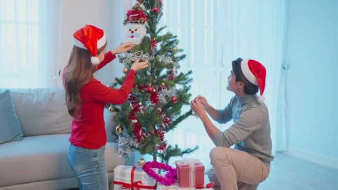 亚洲美丽的情侣在家用幸福装饰圣诞树。有魅力的女人和男人在家里的客厅一起庆祝节日圣诞节感恩派对感到高兴