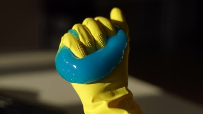 戴着手套准备清洁电脑键盘的无法辨认的人手里的皱巴巴的蓝色粘液吸收凝胶的特写高角度视图。