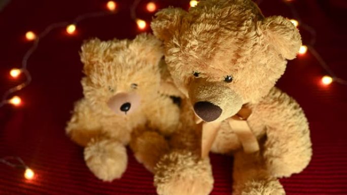 一对泰迪熊正坐在红色针织格子和灯泡花环的背景下。情人节