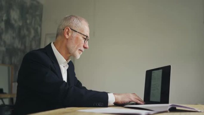 老商人正在打字，处理文件和笔记本电脑。验证数据。