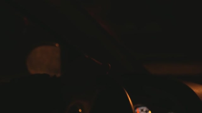 男子双手从车辆内部握着汽车方向盘，在夜路背景下行驶，红绿灯眩光