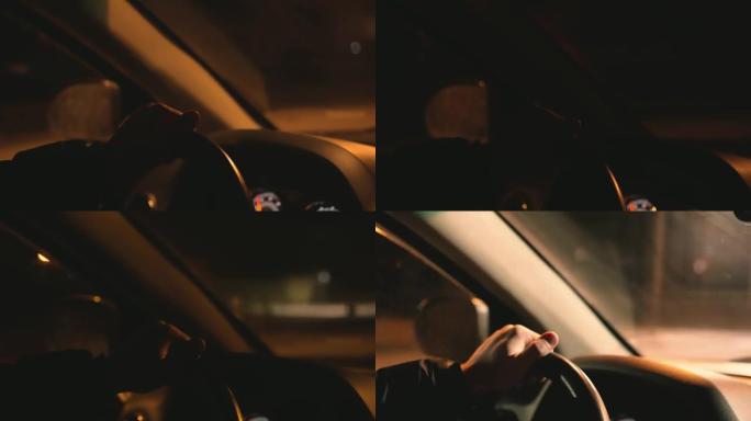 男子双手从车辆内部握着汽车方向盘，在夜路背景下行驶，红绿灯眩光