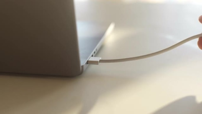 无法识别的人的特写手将现代笔记本电脑中的磁性usb-c电源线插在桌子上。插头插入笔记本电脑电源适配器