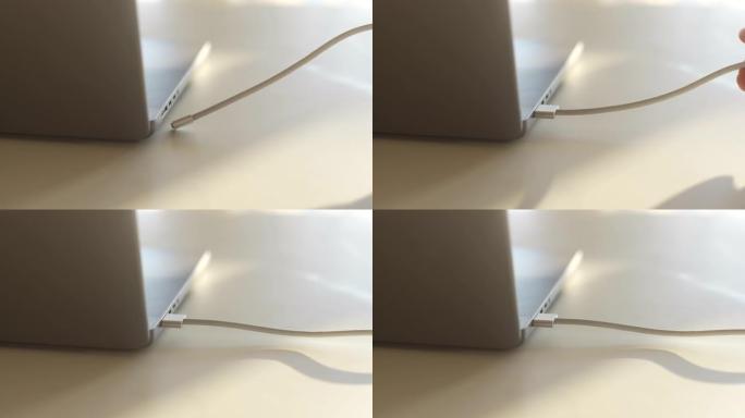 无法识别的人的特写手将现代笔记本电脑中的磁性usb-c电源线插在桌子上。插头插入笔记本电脑电源适配器