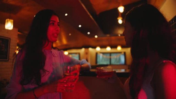 两个年轻快乐美丽的南亚女孩在酒吧聊天和喝酒的特写镜头