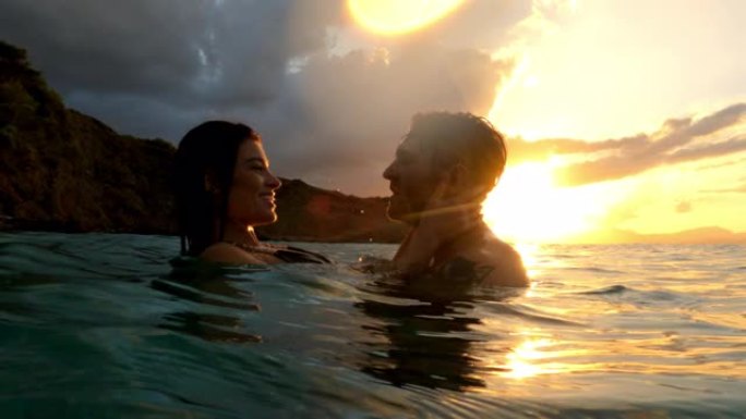 浪漫的异性恋夫妇一起在橙色日落时在海里游泳。在水中接吻