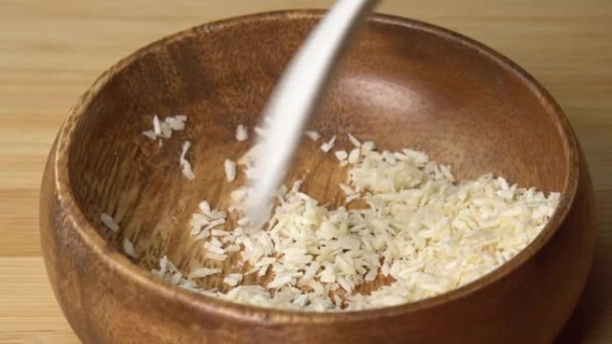 勺子从木碗中捡起椰子片，然后在木板上旋转。椰子屑或磨碎的椰子旋转