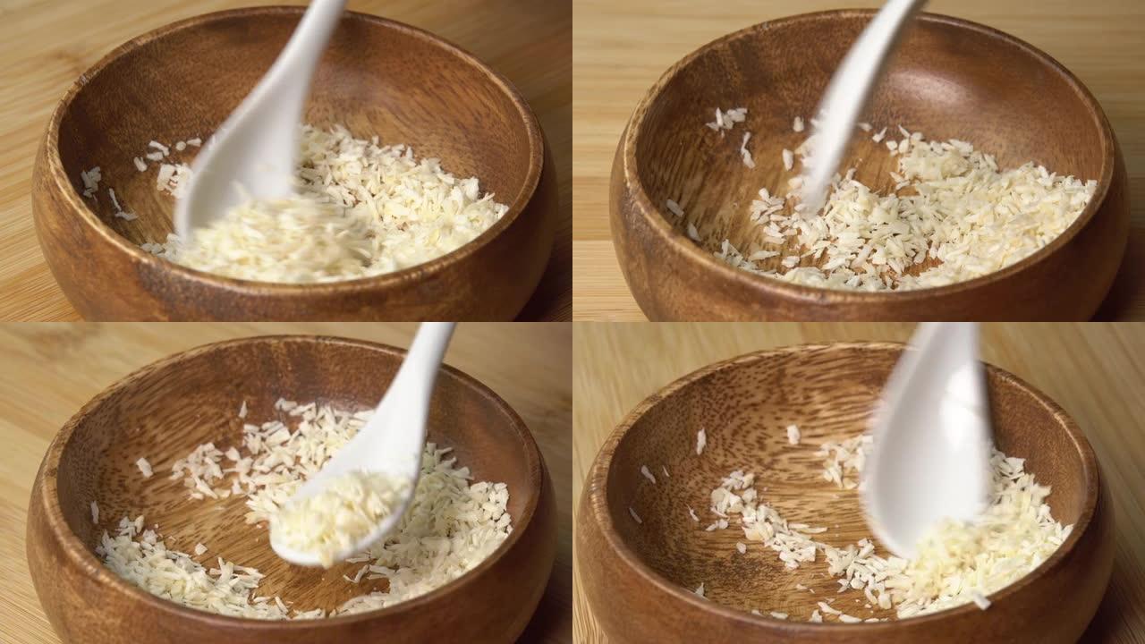 勺子从木碗中捡起椰子片，然后在木板上旋转。椰子屑或磨碎的椰子旋转