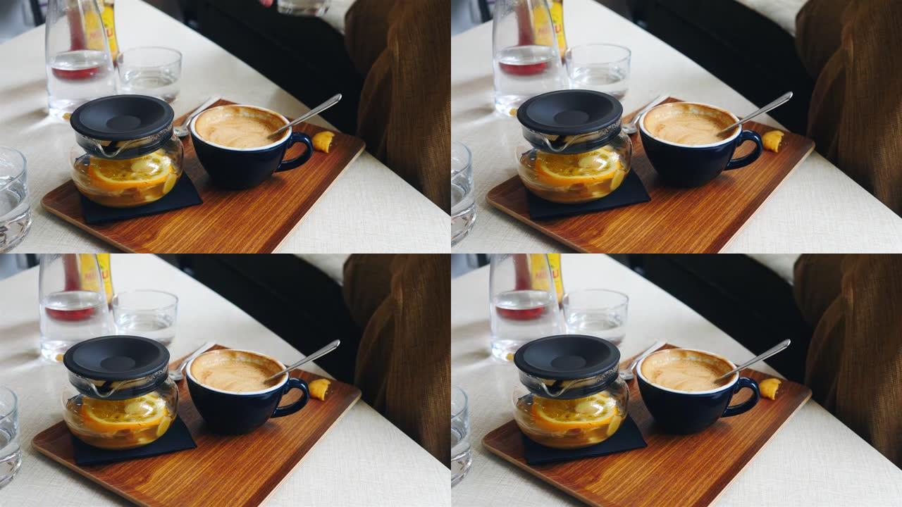 女人在咖啡吧里喝新鲜的生姜和橙茶，在灰色桌子上放一杯咖啡和水
