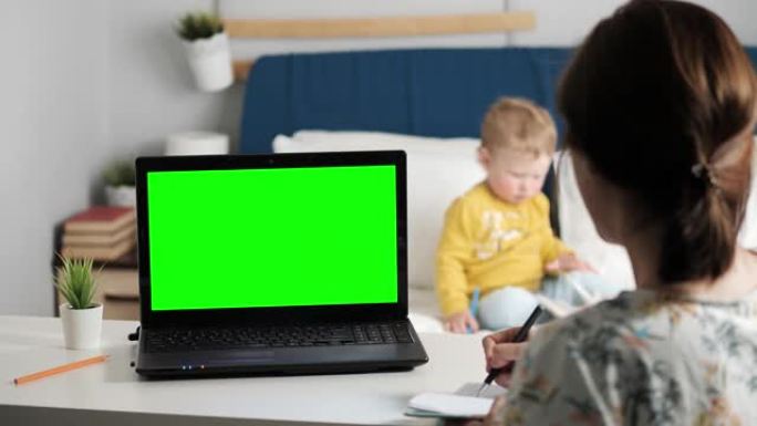 女人坐在卧室的桌子上，看着笔记本电脑的绿屏，通过互联网视频通信与某人交谈，有时在笔记本上做笔记。背景