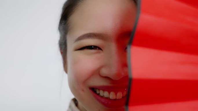 中国/亚洲美女脸特写春节红扇遮住左半边脸，微笑着看着镜头