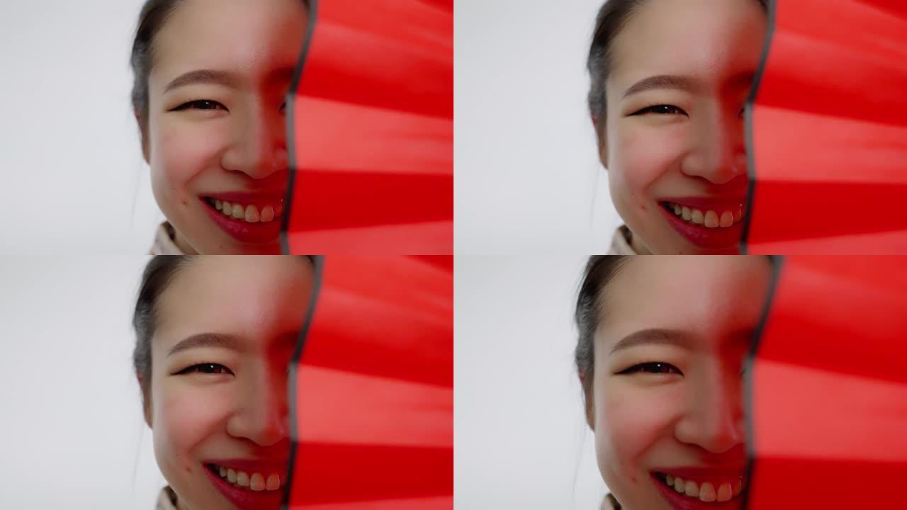 中国/亚洲美女脸特写春节红扇遮住左半边脸，微笑着看着镜头