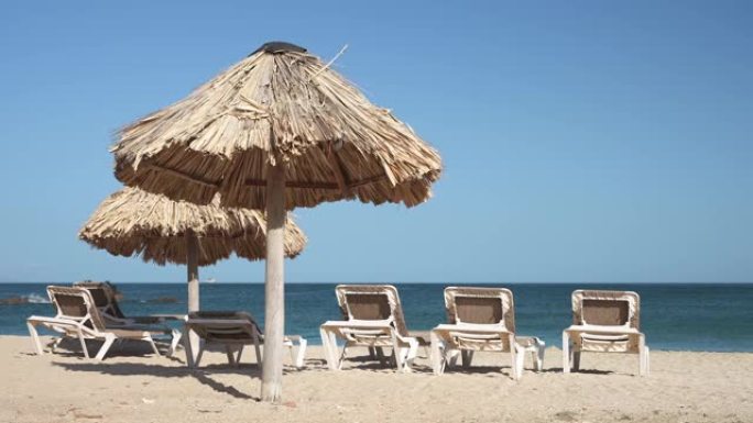 黎明时分无人的沙滩上撑着草伞，还有一排空荡荡的躺椅。在美丽的海滨度假