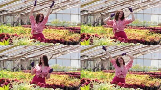 一个穿着红色衬衫的年轻女孩正在温室里跳舞。周边有盆栽花的工业温室。