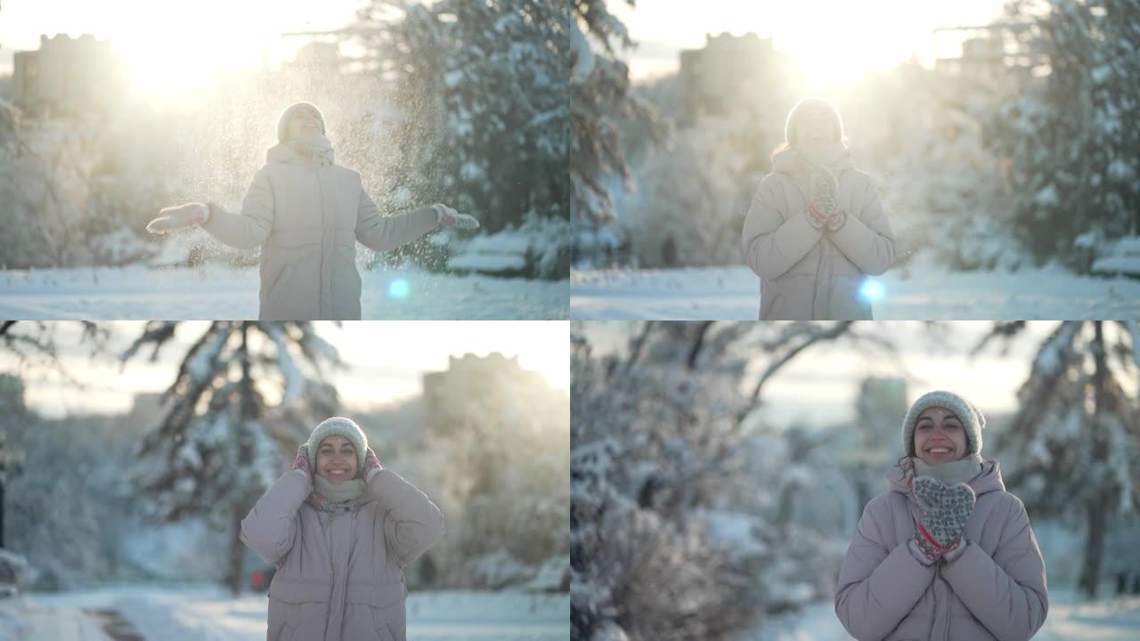 穿着暖和衣服的顽皮年轻女子在阳光明媚的冬季白雪皑皑的公园里撒雪，围着她转，用雪花拍手