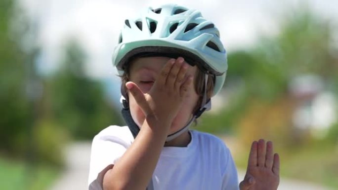 戴头盔的孩子用手摩擦脸的肖像。骑自行车的男孩擦鼻子