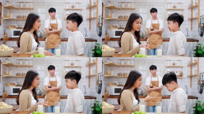 年轻的亚洲男孩站在厨房里，母亲责骂儿子不喝牛奶。父亲站在后面，看着家人。不快乐的男孩不喜欢吃早餐。周