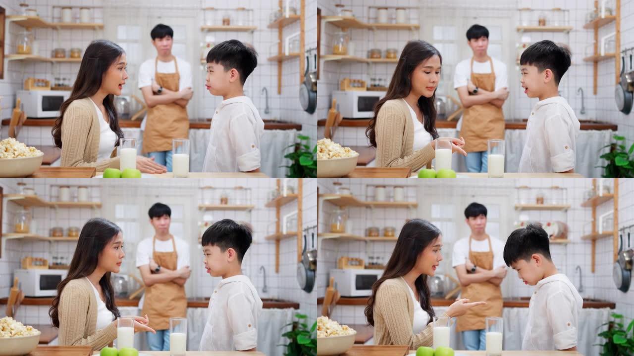 年轻的亚洲男孩站在厨房里，母亲责骂儿子不喝牛奶。父亲站在后面，看着家人。不快乐的男孩不喜欢吃早餐。周