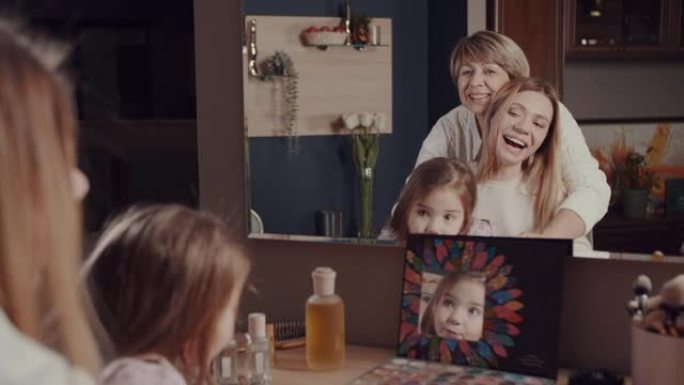 一个幸福家庭的三代女人，一个老奶奶，一个小女儿和一个小女孩在镜子前拥抱，微笑，大笑。生动的情感。一个