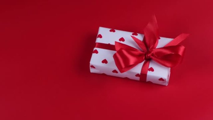 旋转礼品盒包裹在纸心和红色背景上的红色蝴蝶结情人节庆祝概念