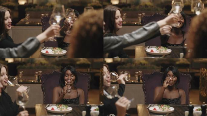 快乐的非洲和高加索妇女在餐厅庆祝生日或圣诞节，碰杯