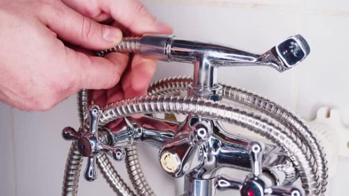 修理工把淋浴软管拧到水龙头上。水管工的手特写。