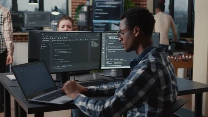 专注的程序员在坐在带多个屏幕的笔记本电脑上打字时固定眼镜