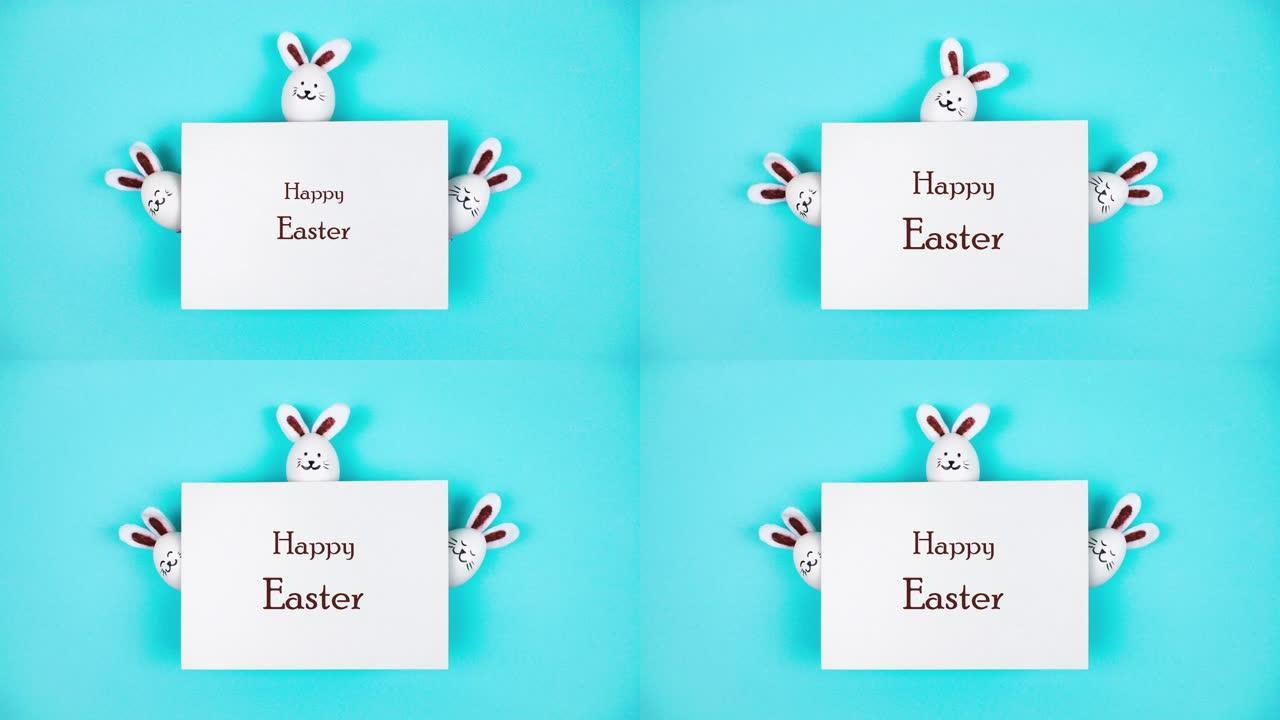 三个由白鸡蛋制成的复活节兔子从一张白纸后面冒出来。节日贺卡 “复活节快乐”。