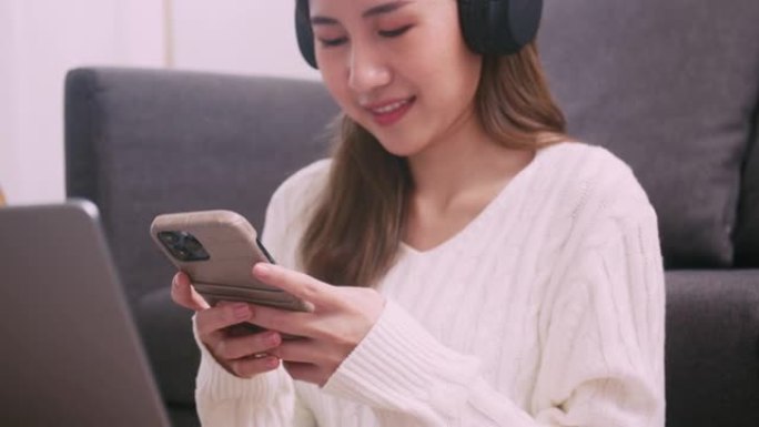 美丽的亚洲女人坐在客厅时使用手机滚动社交媒体提要。