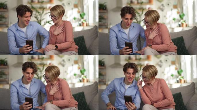 母亲和成年儿子坐在沙发上在家中使用智能手机