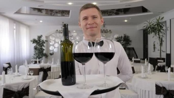 一位男服务员在一家餐馆里拿着一个装有红酒的托盘。