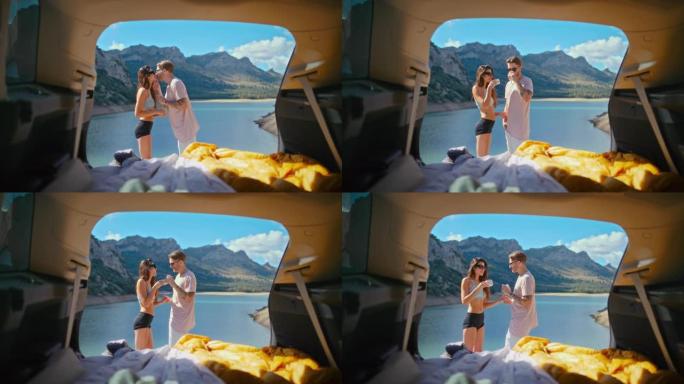 亲爱的夫妇在湖边的一个大汽车后备箱里休息和露营。欣赏湖景，喝茶