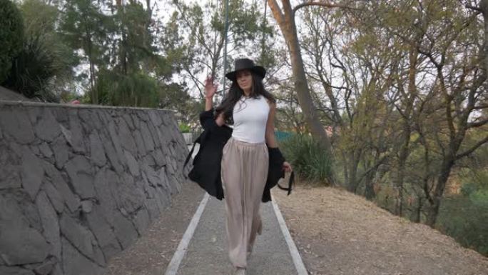 一个西班牙裔模特戴着帽子在公园走秀的漂亮4k镜头