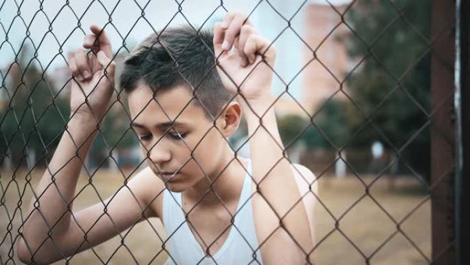 难民男孩独自一人低头在篱笆附近，沮丧的男孩垂下了眼睛，后悔了这一举动，电影拍摄