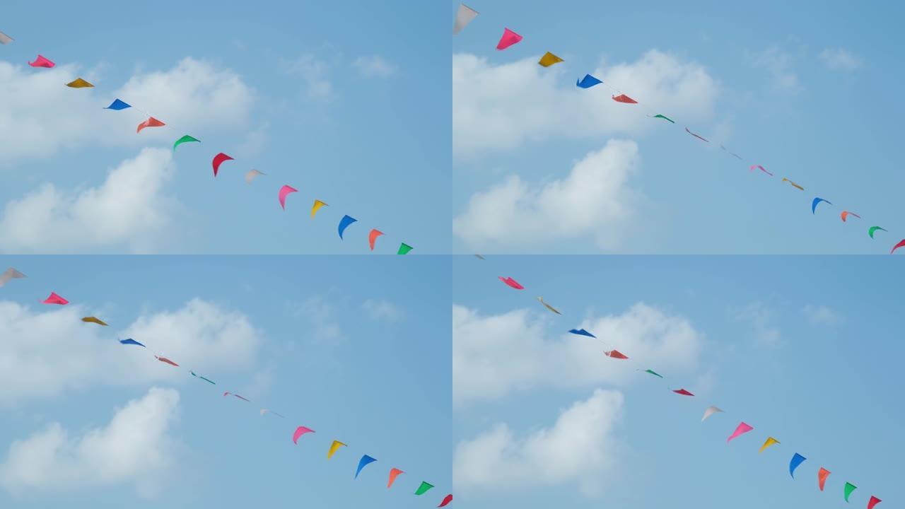 彩色的小旗子在天空中飘扬。在蓝天的映衬下，挥舞着挂在绳子上的小彩旗庆祝节日。