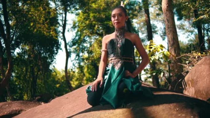 一位穿着绿色服装的美丽亚洲妇女坐在一块大石头上，参观村庄内的森林