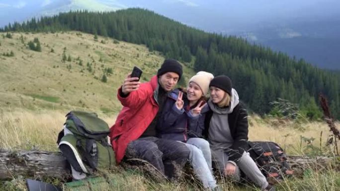 一群徒步旅行者在山顶停下来时坐在一棵倒下的树上，并使用该应用程序在智能手机上拍照和拍照。