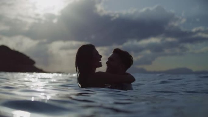 浪漫的异性恋情侣一起在金色日落时在海里游泳。拥抱