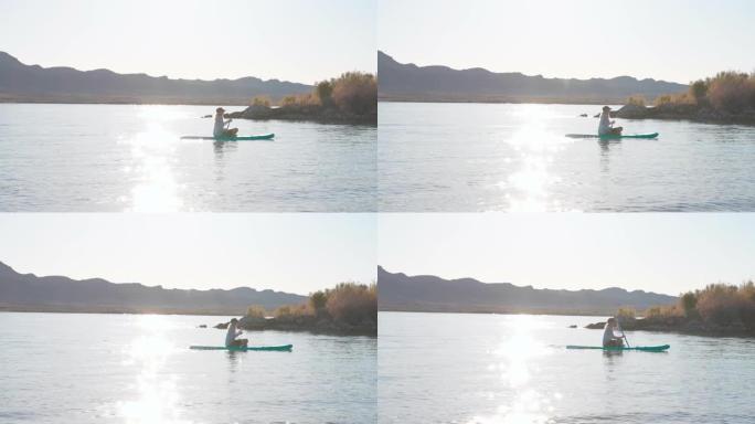 成熟的女人在平静的湖上划桨充气SUP