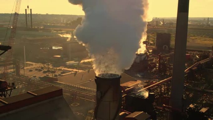 日落时间和黄金时段的钢厂管道。浓烟背后的阳光。冶金厂和烟云来自烟囱，形成温室气体区层。气候变化。