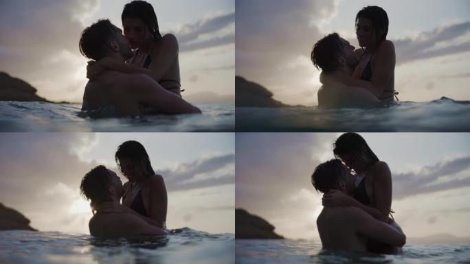 暑假浪漫的异性恋夫妇。在美丽的金色日落时在海里游泳。温柔地拥抱