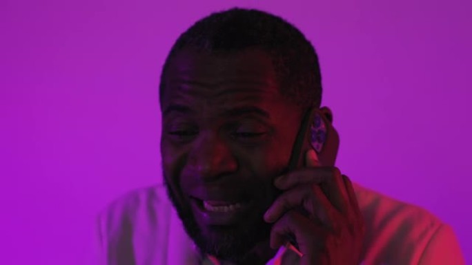 黑人坐在智能手机上聊天。非裔美国人在演播室通过电话吵架挂断了电话。紫罗兰色洋红色背景。特写镜头