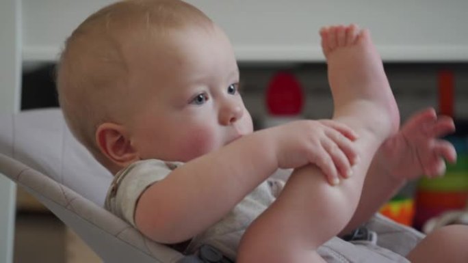 男婴抱着他的赤脚，10个月大的高加索孩子在婴儿摇椅上玩他的赤脚特写